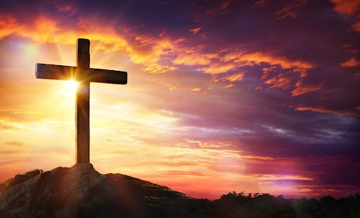 Cross At Sunset With Sunlight And Orange Clouds